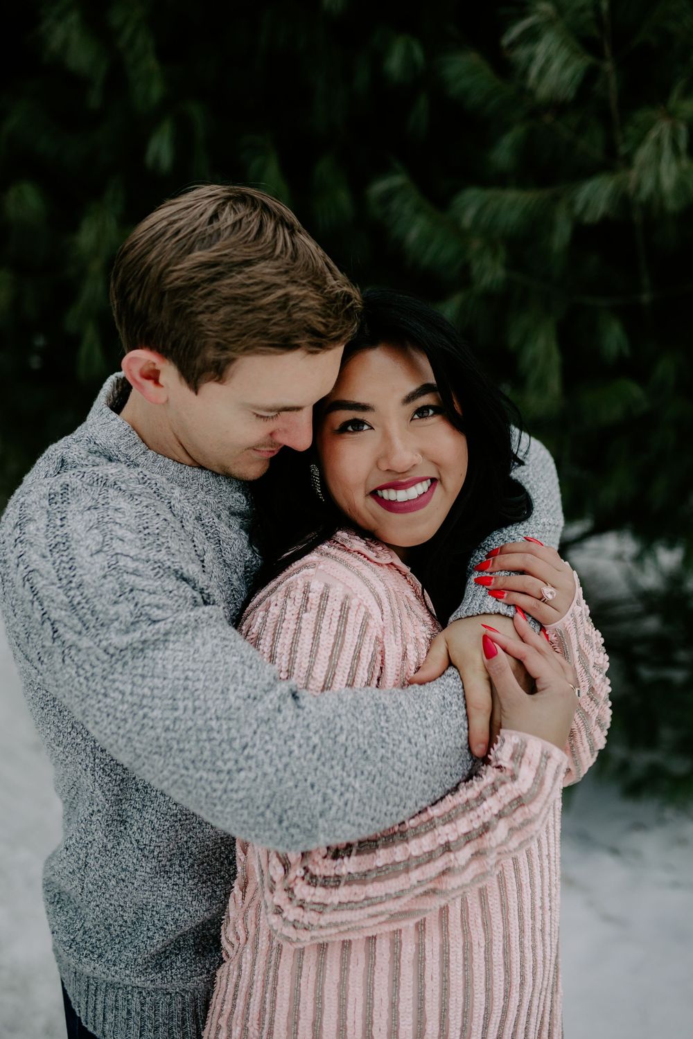 A couple shares an intimate moment wearing coordinated knit sweaters against a snowy backdrop.