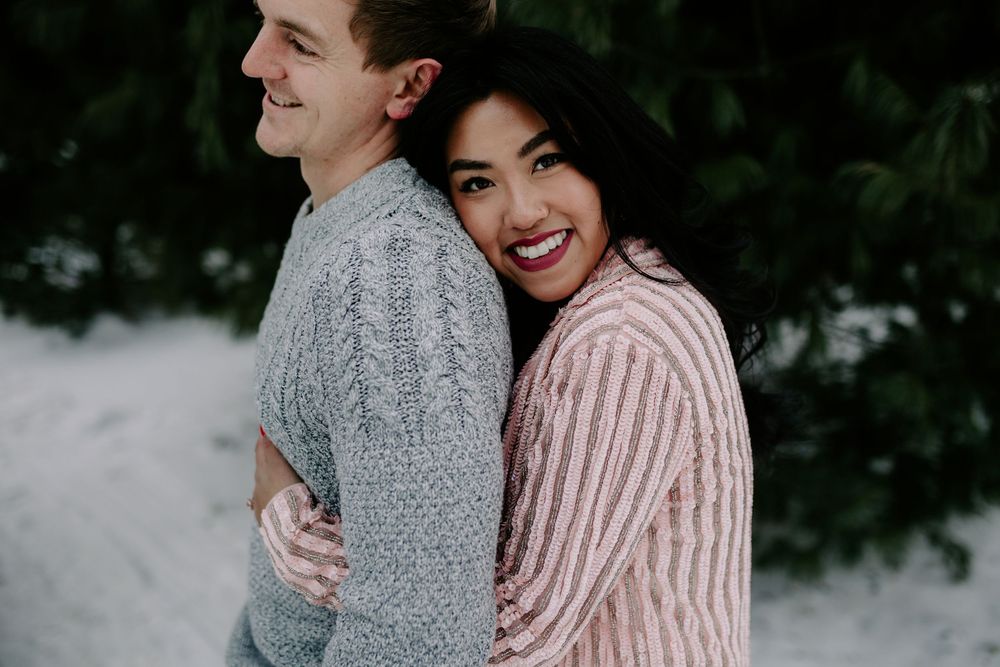 A happy couple in winter attire shares a joyful moment against a snowy background.