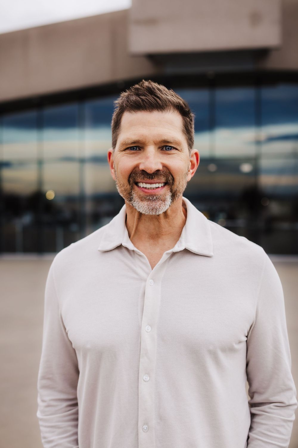 Professional portrait of person in white button-down shirt against modern building exterior.