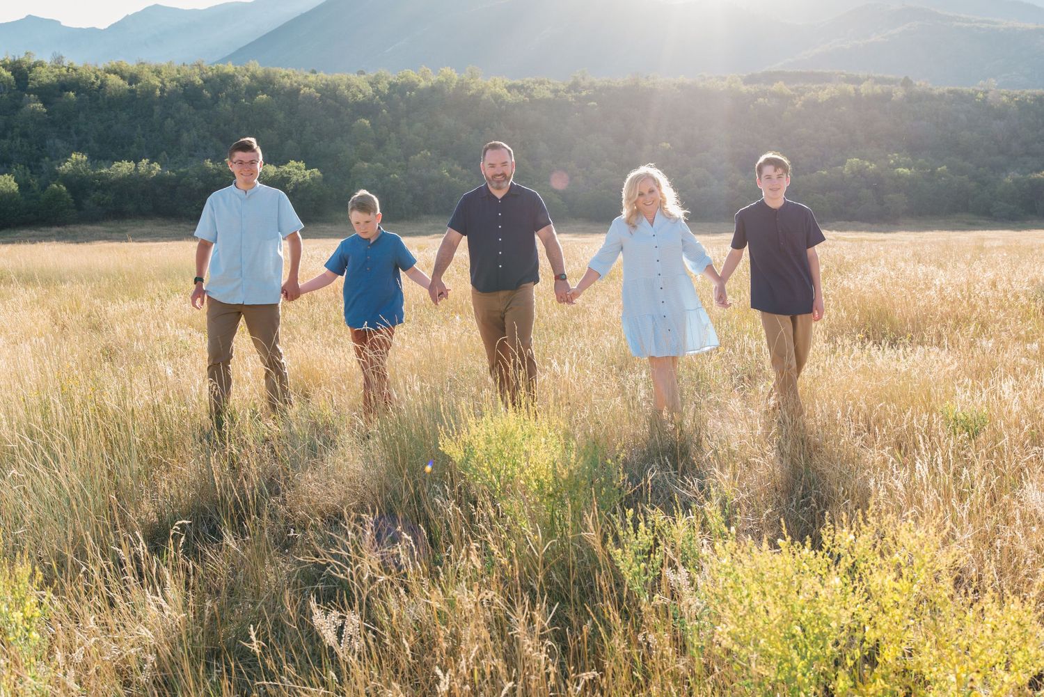 Group of people holding hands in sunlit field with mountains in background.