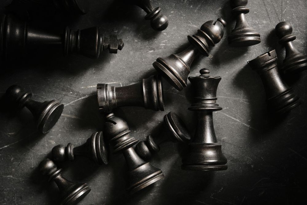 Old black wooden chess pieces are scattered on a dark stone background with atmospheric side lighting.