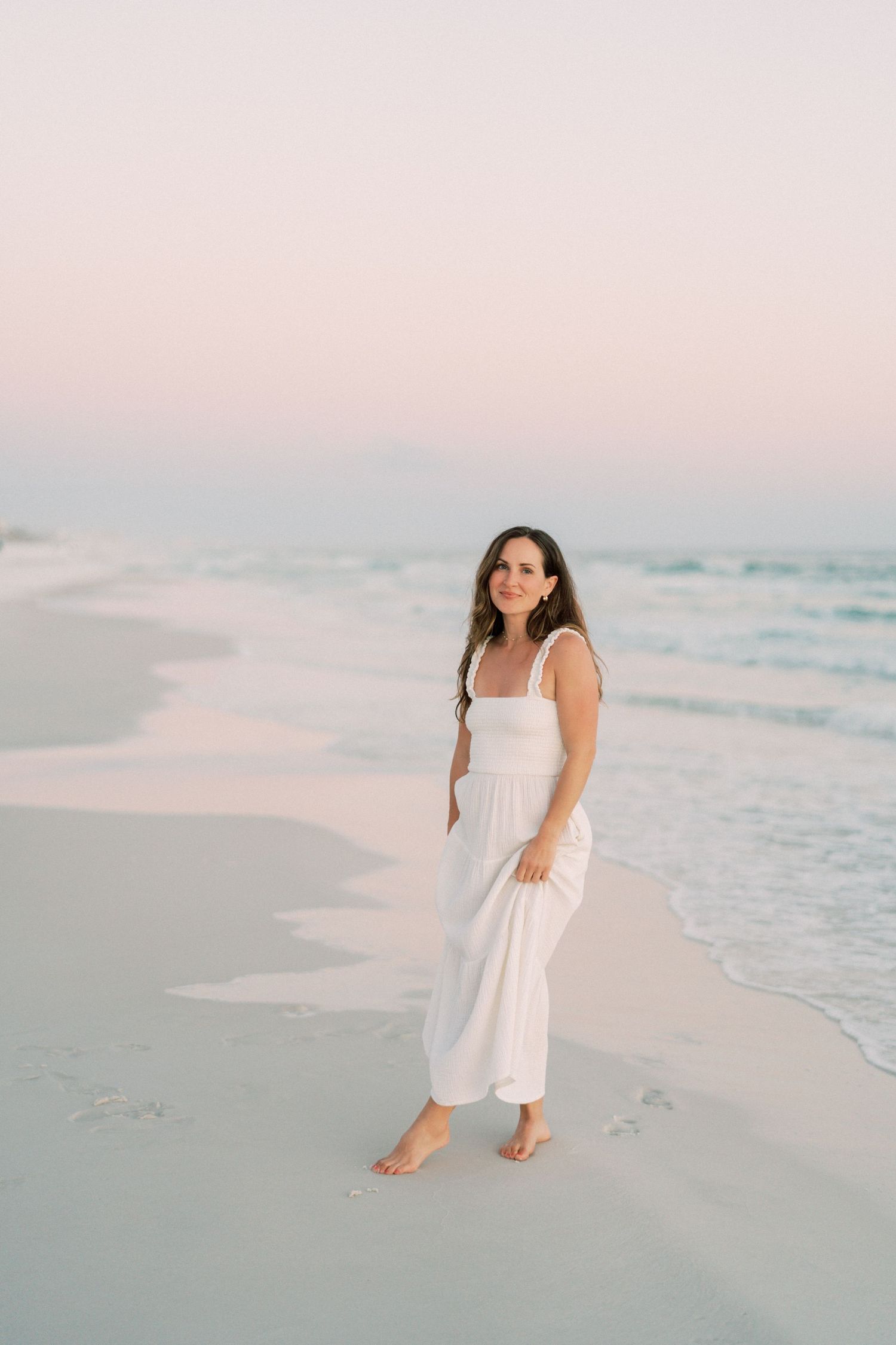Professional photographer in a flowing white dress holds a DSLR camera while standing outdoors on a sunny day.