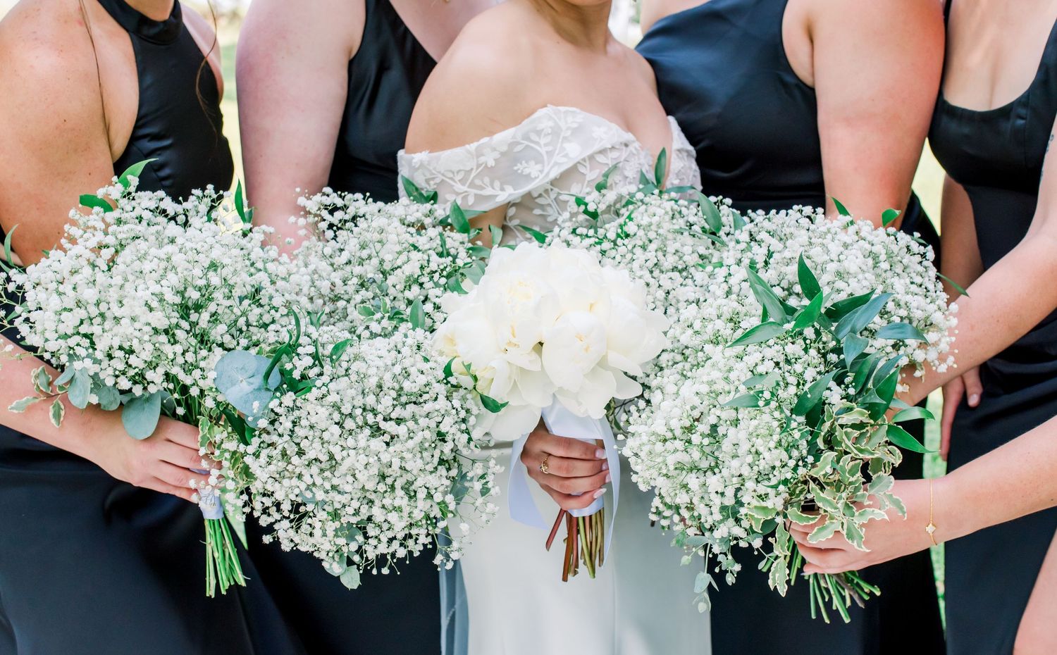 Bridesmaids holding delicate baby's breath bouquets against black dresses at an outdoor wedding.