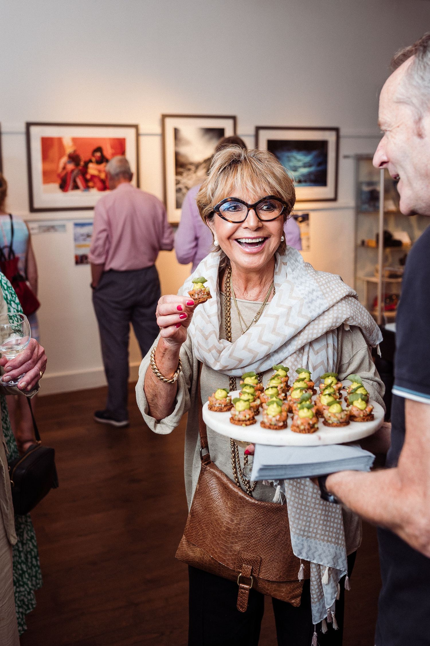 A series of photos showing appetizers being served at an art gallery reception with people mingling in the background.
