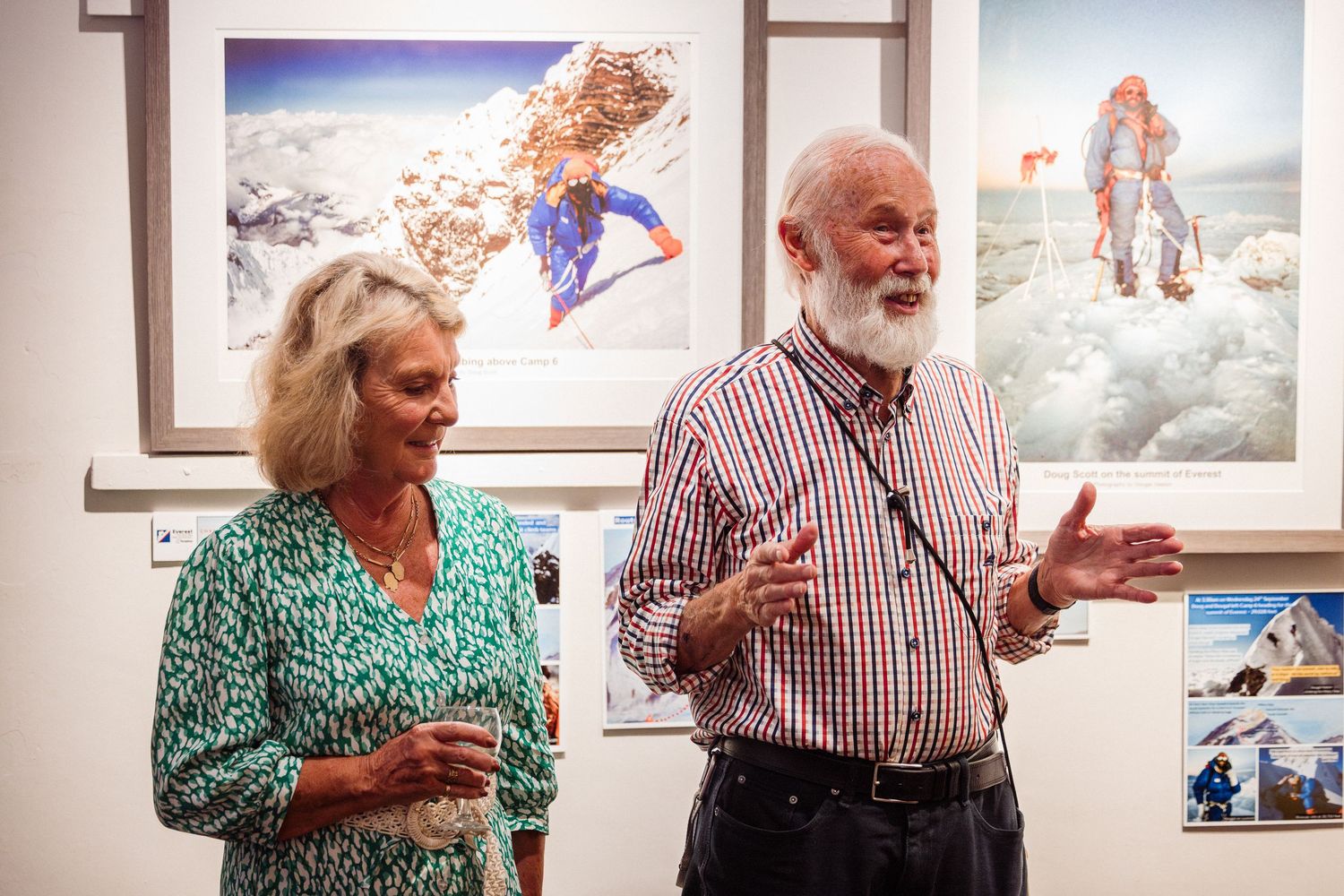 Elderly couple laughs and gestures while having an animated conversation in front of artwork at a gallery.