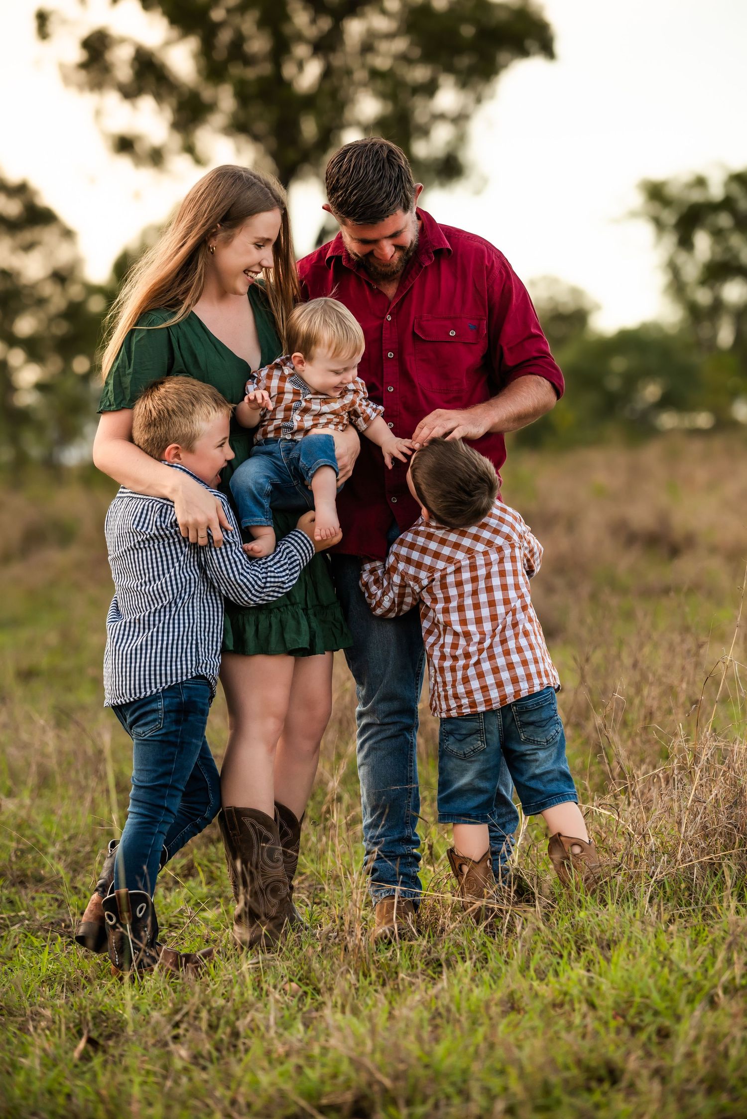 A family shares an intimate moment together in a field at sunset, with three children and two adults in casual attire.
