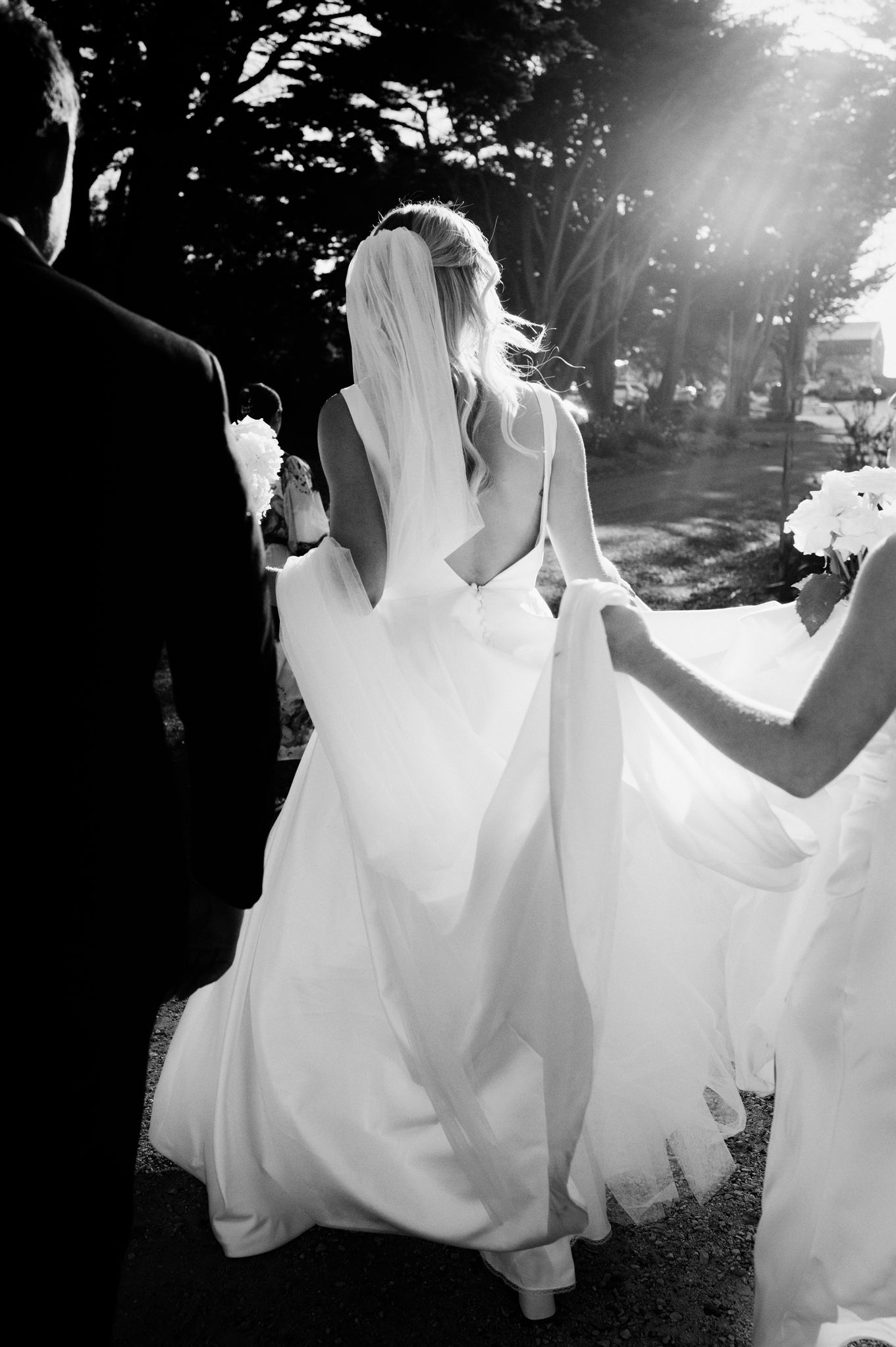 Black and white candid moment of bride walking in sunlit garden.