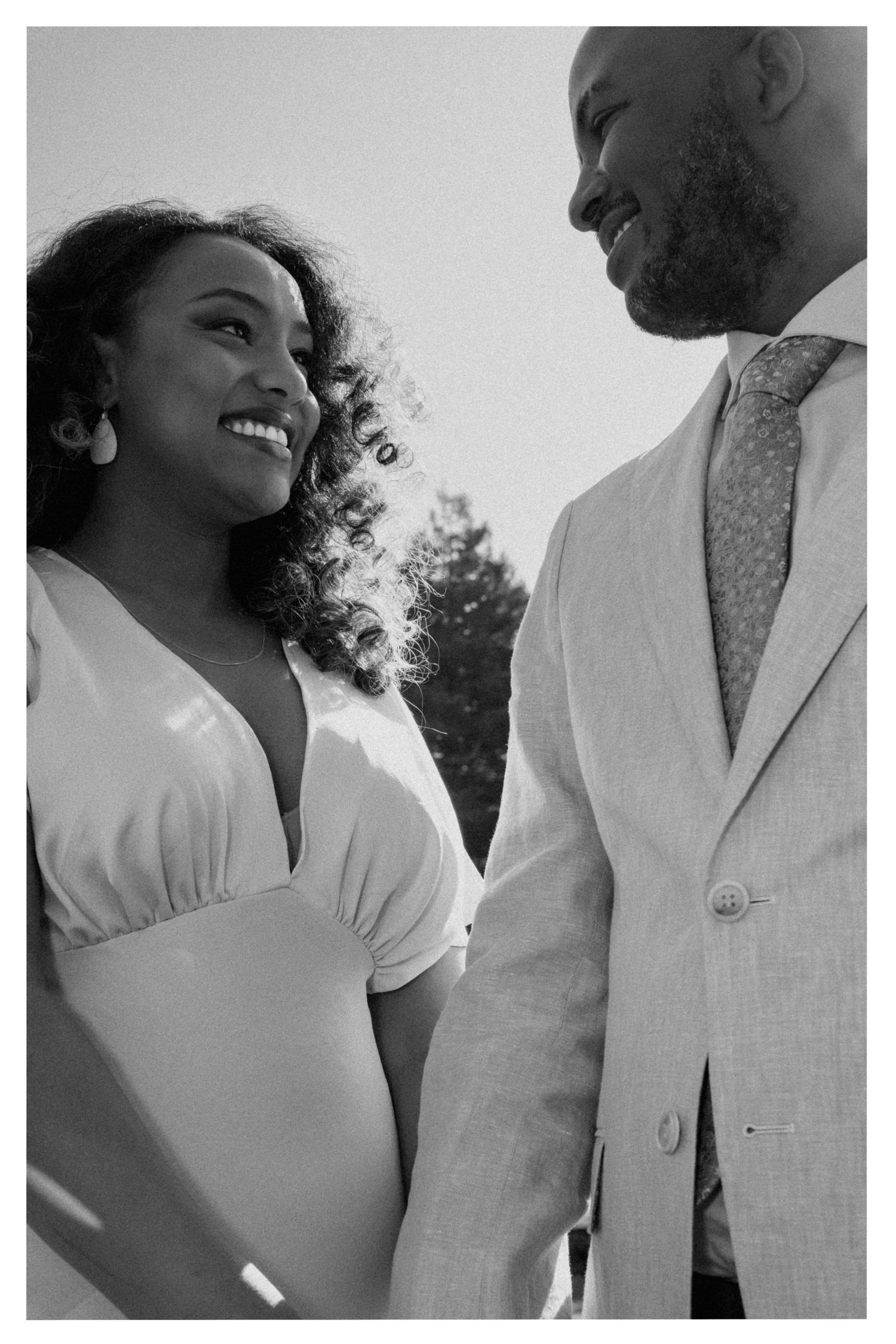 A black and white photo of a couple sharing a joyful moment together outdoors in formal attire.