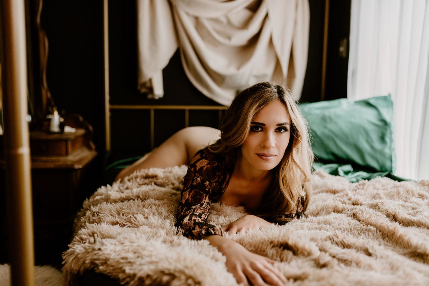 Intimate boudoir photo featuring a person lying on a plush beige blanket in moody lighting.