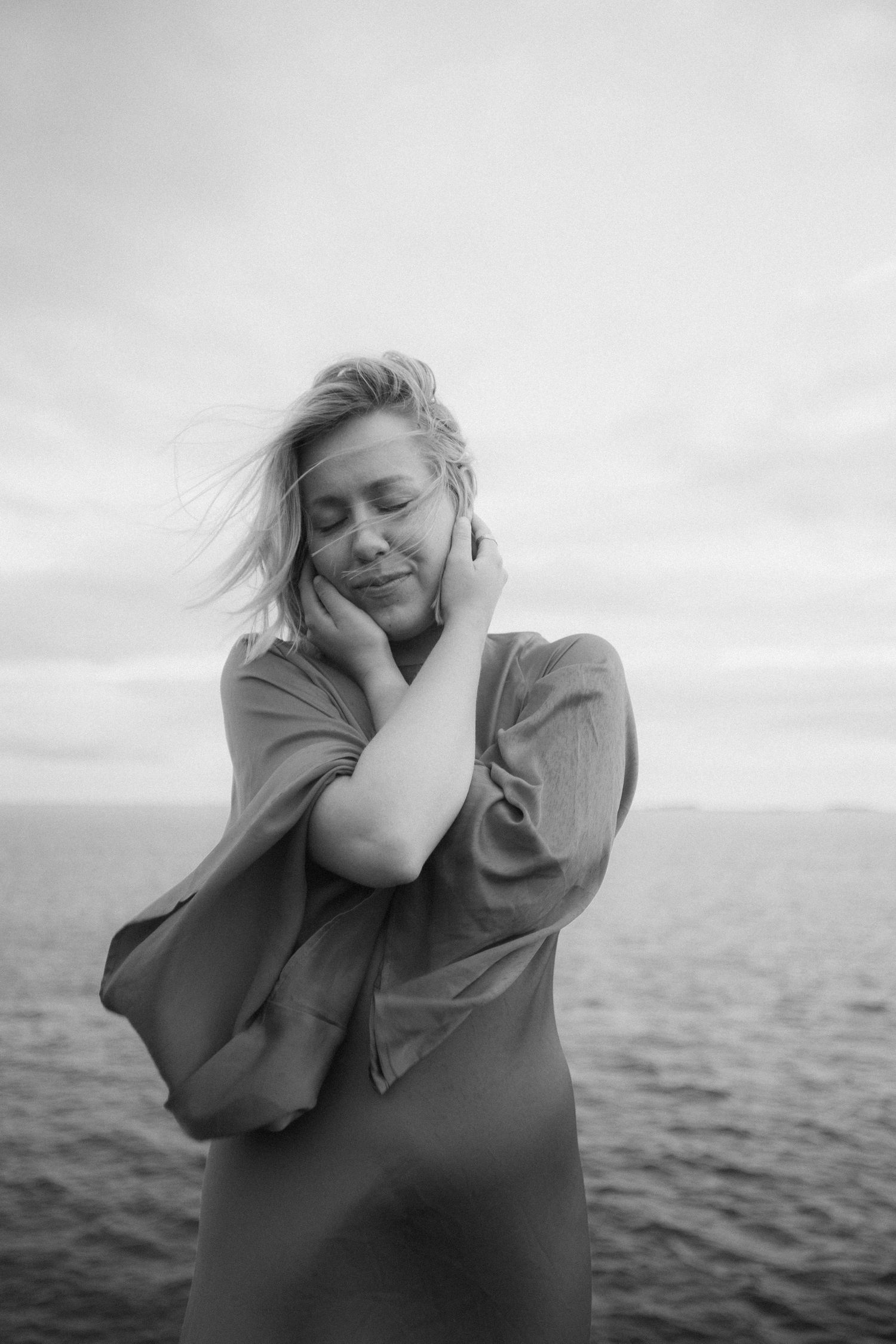 A black and white portrait of a woman with windswept hair by the ocean.