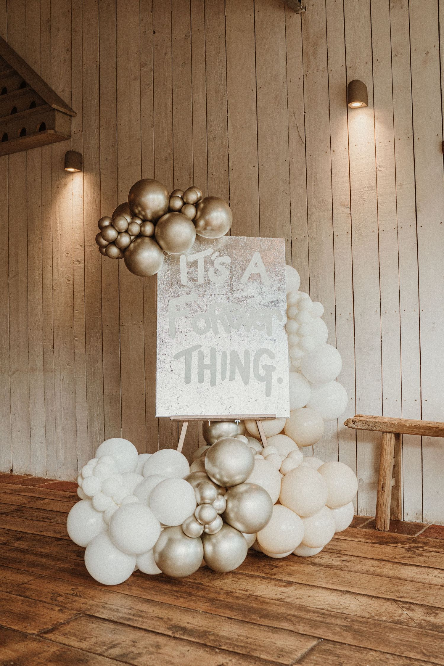 White and silver balloon decorations with 'It's A Thing' sign on rustic wooden backdrop.