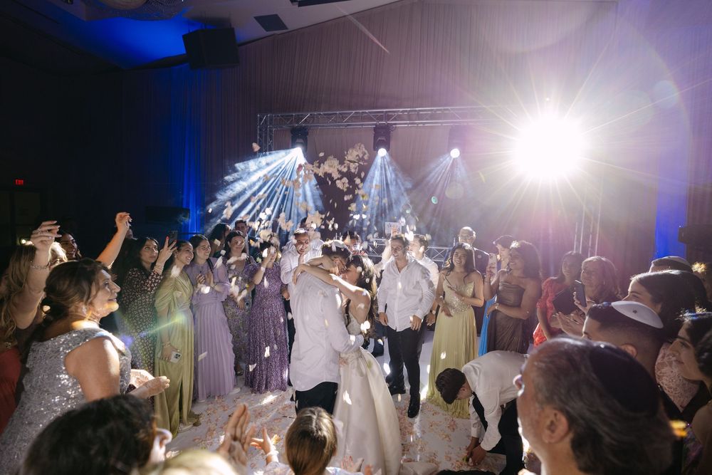 A festive wedding celebration on the dance floor with blue mood lighting and people dancing and celebrating together.