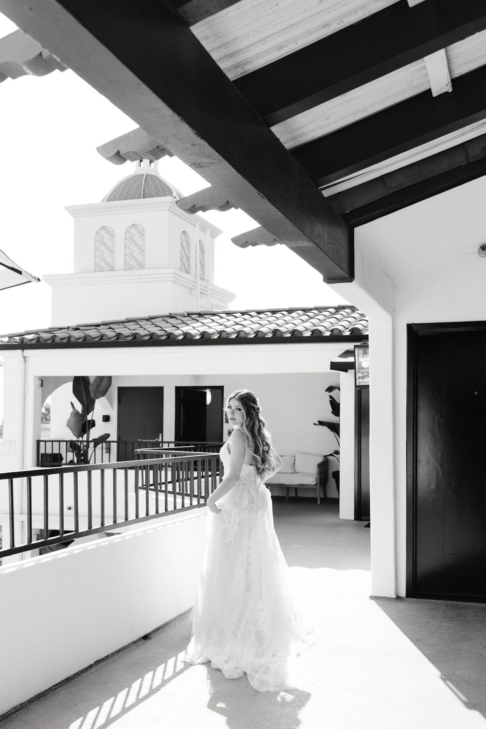A bride in a flowing white gown creates a graceful silhouette against a bright white hallway with dramatic shadows.