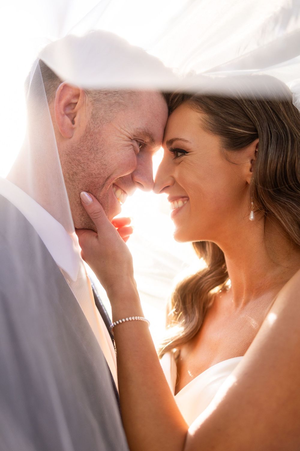 Sunlit close-up of couple sharing intimate moment during wedding photoshoot.