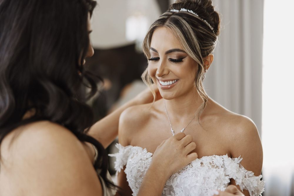 A bride in a white lace dress smiles joyfully while getting ready on her wedding day.