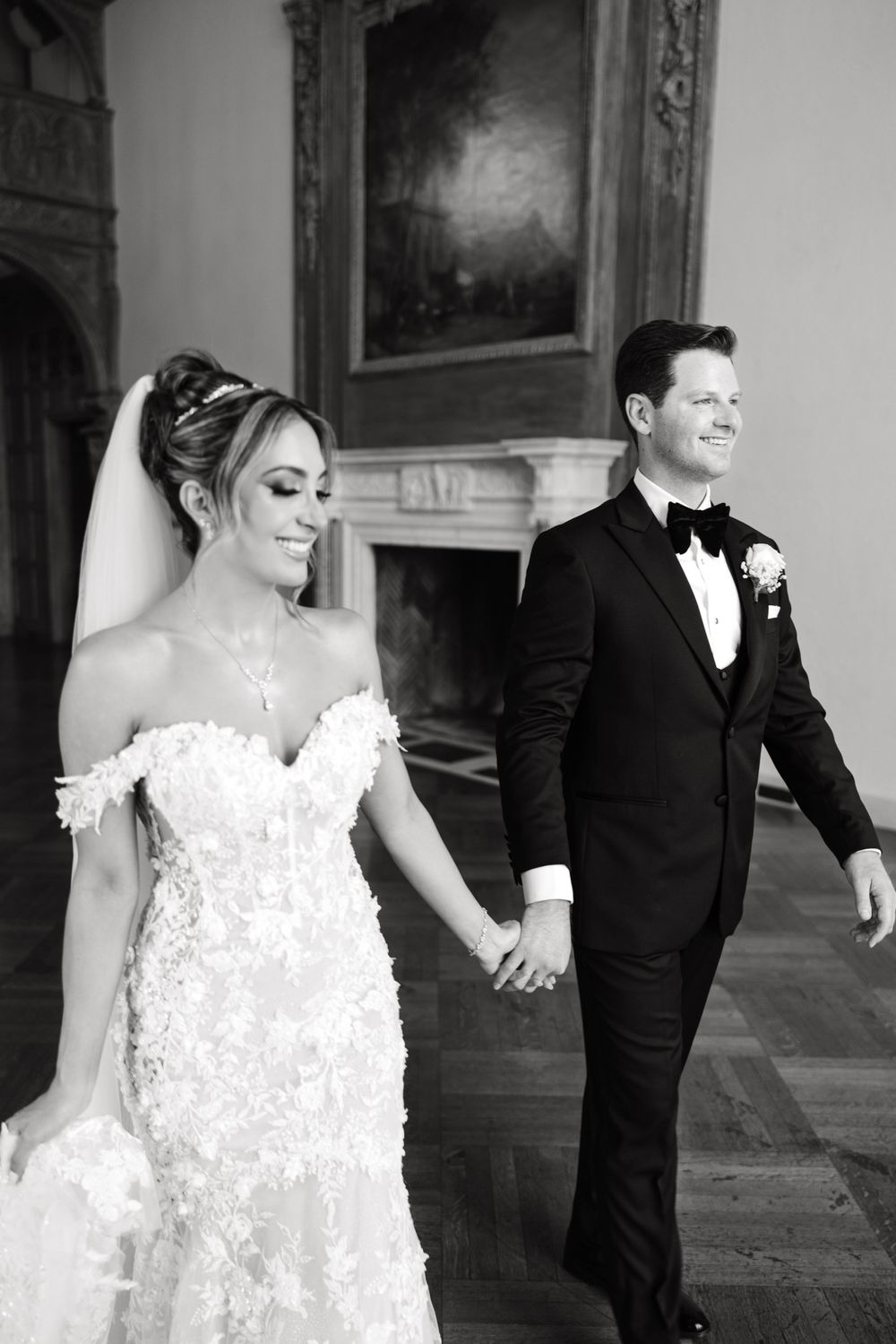 A couple holds hands while walking through an elegant hallway in their wedding attire.