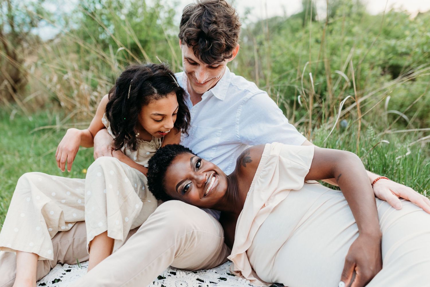 Family lying together and laughing on a blanket in a sun-drenched meadow.