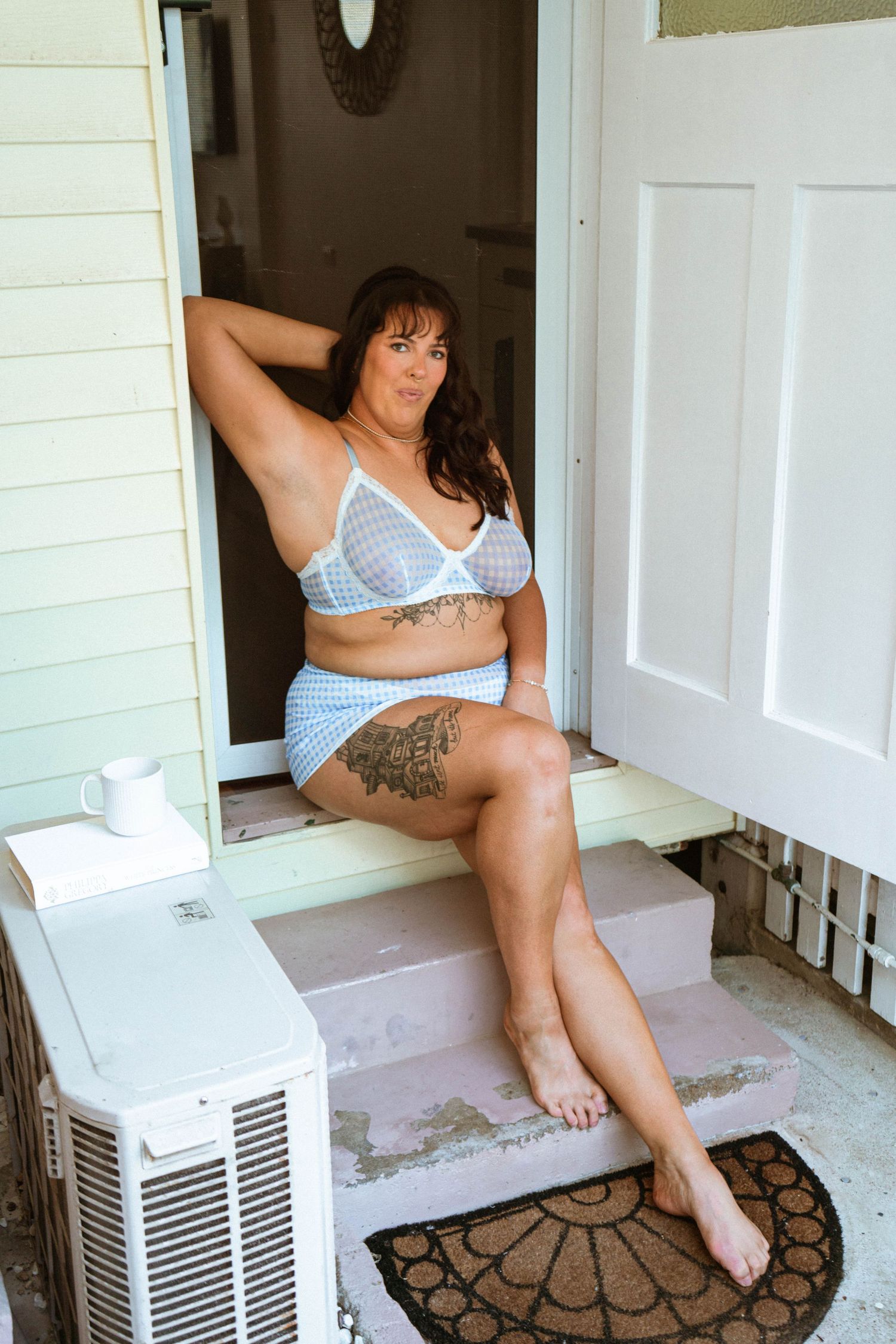 Woman in blue gingham lingerie set sitting on porch steps, showcasing plus-size fashion with tattoos.  Cairns boudoir photographer.
