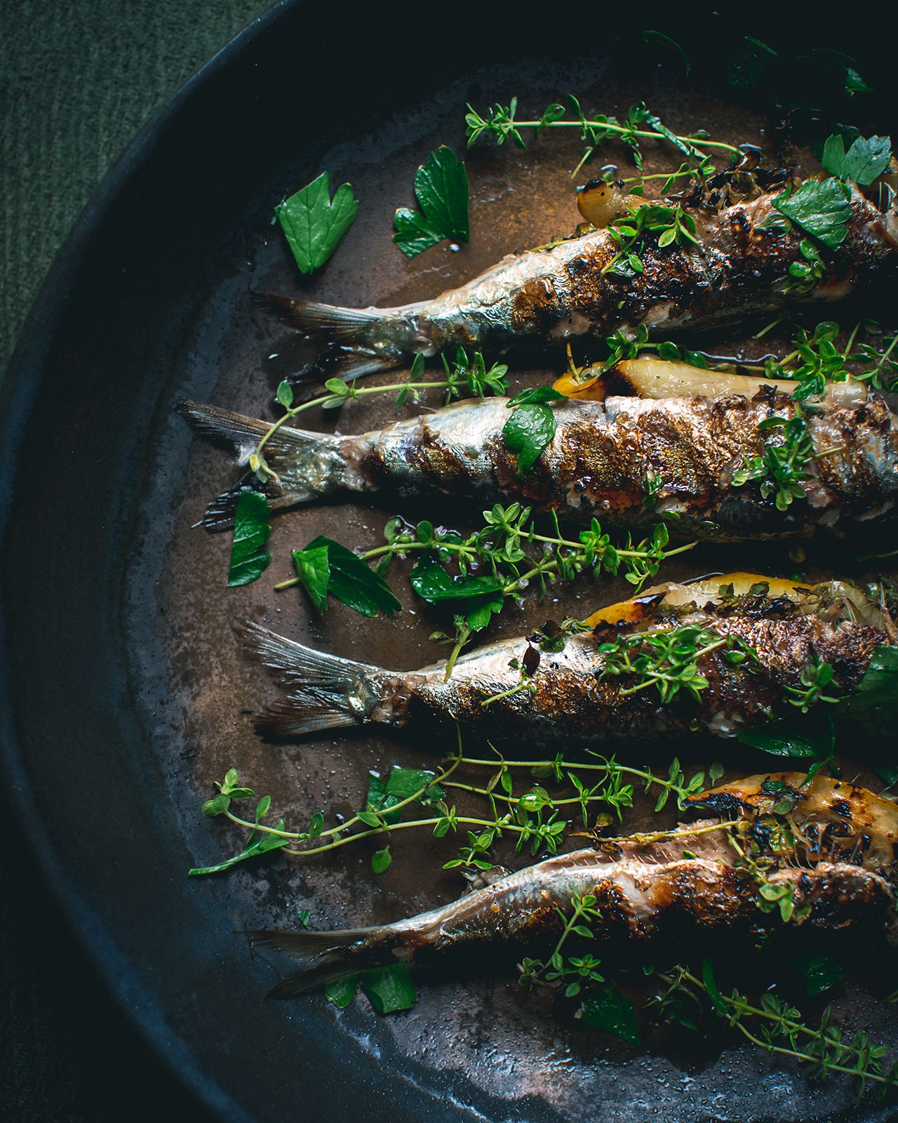 Grilled sardines garnished with fresh herbs and parsley served in a dark cast iron pan.