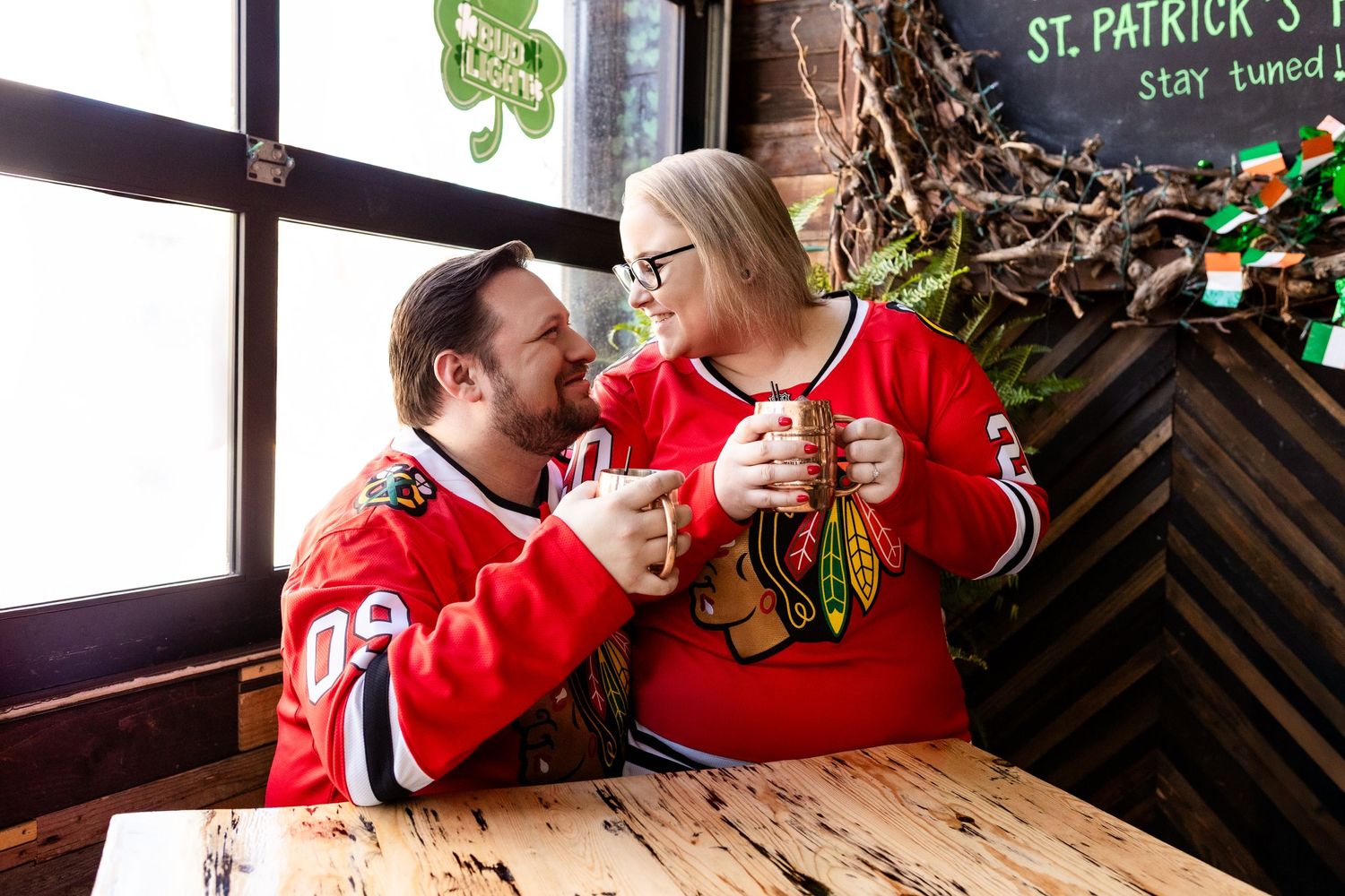 Two people in red Chicago Blackhawks sweaters share a joyful moment at a St. Patrick's Day themed bar.