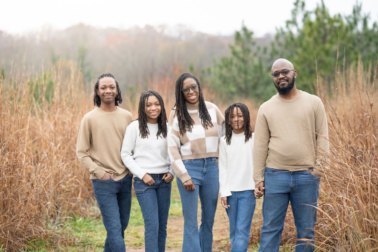Family of five wearing coordinated neutral outfits posing in tall autumn grass.