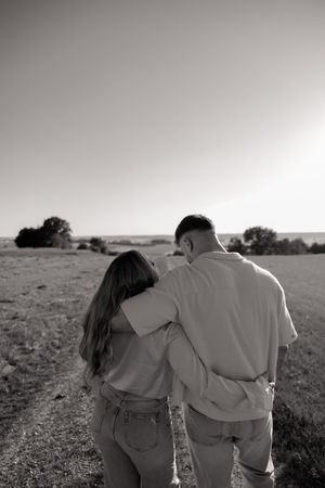 Couple walking together in black and white along an open field path at sunset.