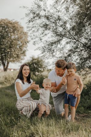 Family playing and laughing together on grassy hill during golden hour.