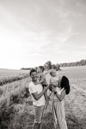 Black and white portrait of family embracing and laughing in sunny meadow.
