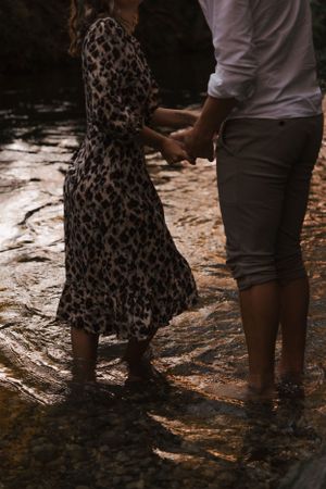 Couple standing in shallow water wearing casual clothes and holding hands.