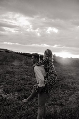 Intimate black and white portrait of a couple sharing a tender moment at sunset in a field.