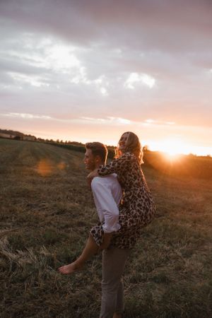 Couple embracing in a golden field during sunset with warm light illuminating the scene.