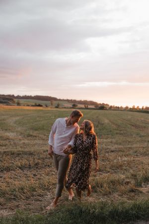 Couple walking hand in hand through a rural field during golden hour sunset.