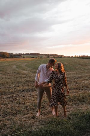 Romantic couple embracing in a rural field during sunset with warm lighting.