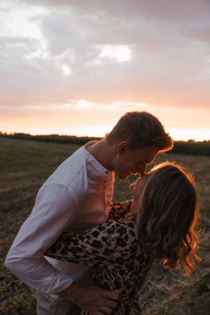 Romantic couple sharing an intimate moment in a field backlit by warm sunset light.