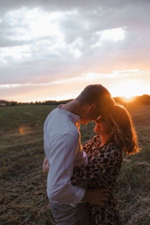 Intimate couple's portrait during golden hour in a field with dramatic sky.