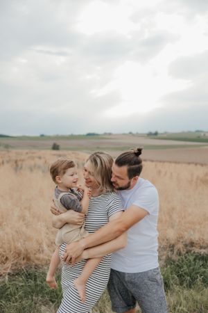 Family embracing and laughing together in a golden wheat field under cloudy skies.