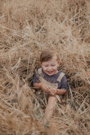 Young child playing and laughing in tall golden grass during autumn.