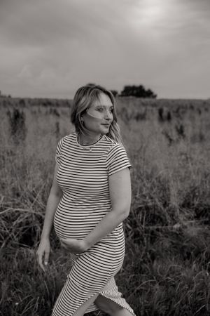Expectant mother in striped dress walking through a misty field at sunset.