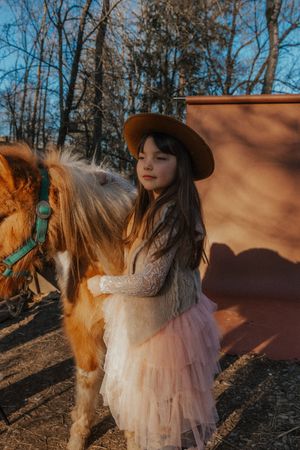 Person in flowing tulle dress poses with horse during golden hour in wooded setting.