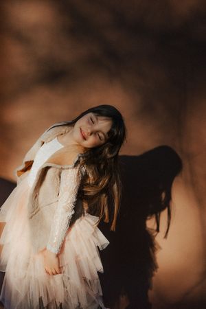 A whimsical portrait in a lace dress against a moody brown backdrop with dramatic shadows.
