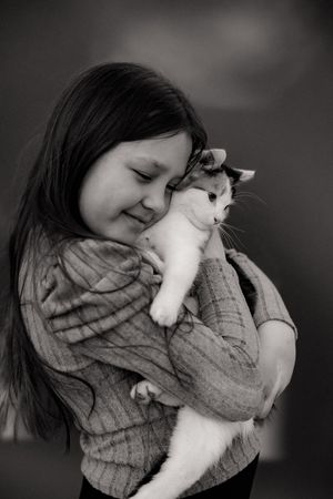 Black and white portrait of someone cuddling with a white cat while wearing a knit sweater.