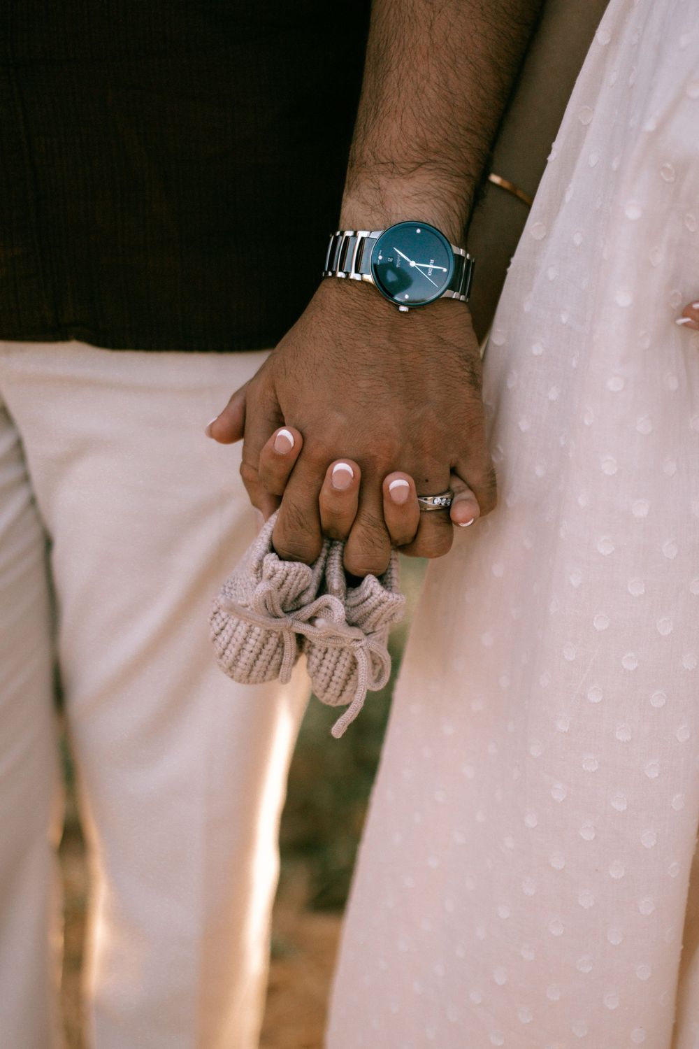 Close-up shot of hands holding each other against a white dress background in soft lighting.