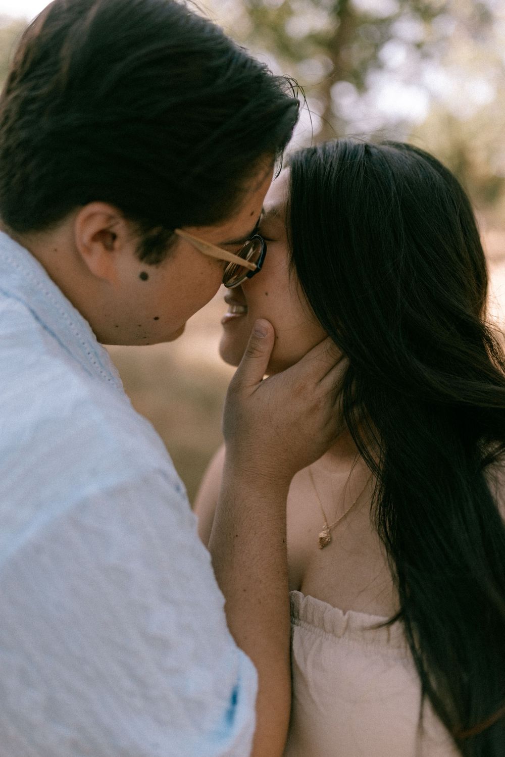 A couple shares an intimate moment, the man tenderly holding the woman's face as they lean in for a kiss outdoors.