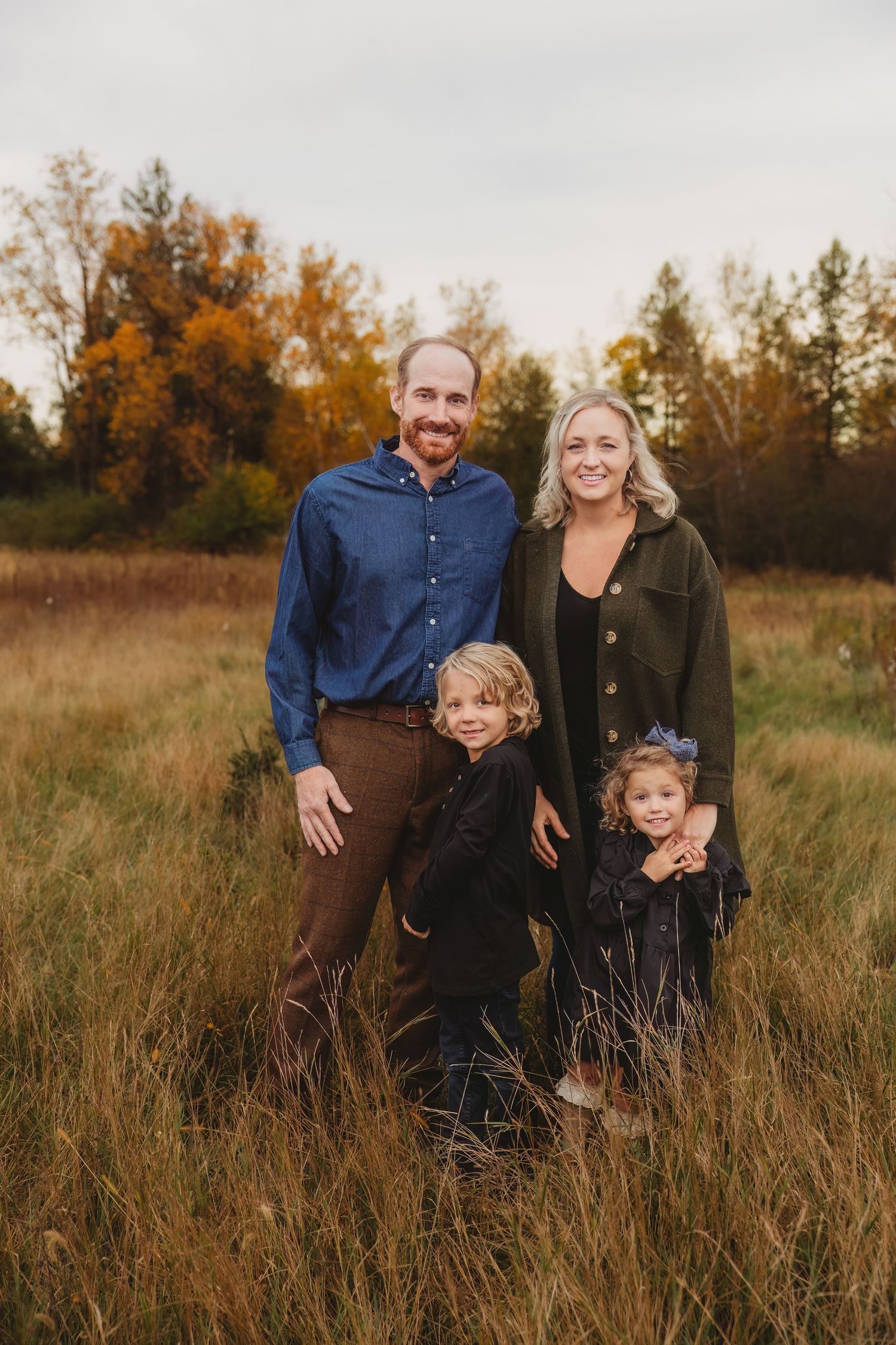 Family in casual summer outfits walking together on a dirt path through a lush green park.