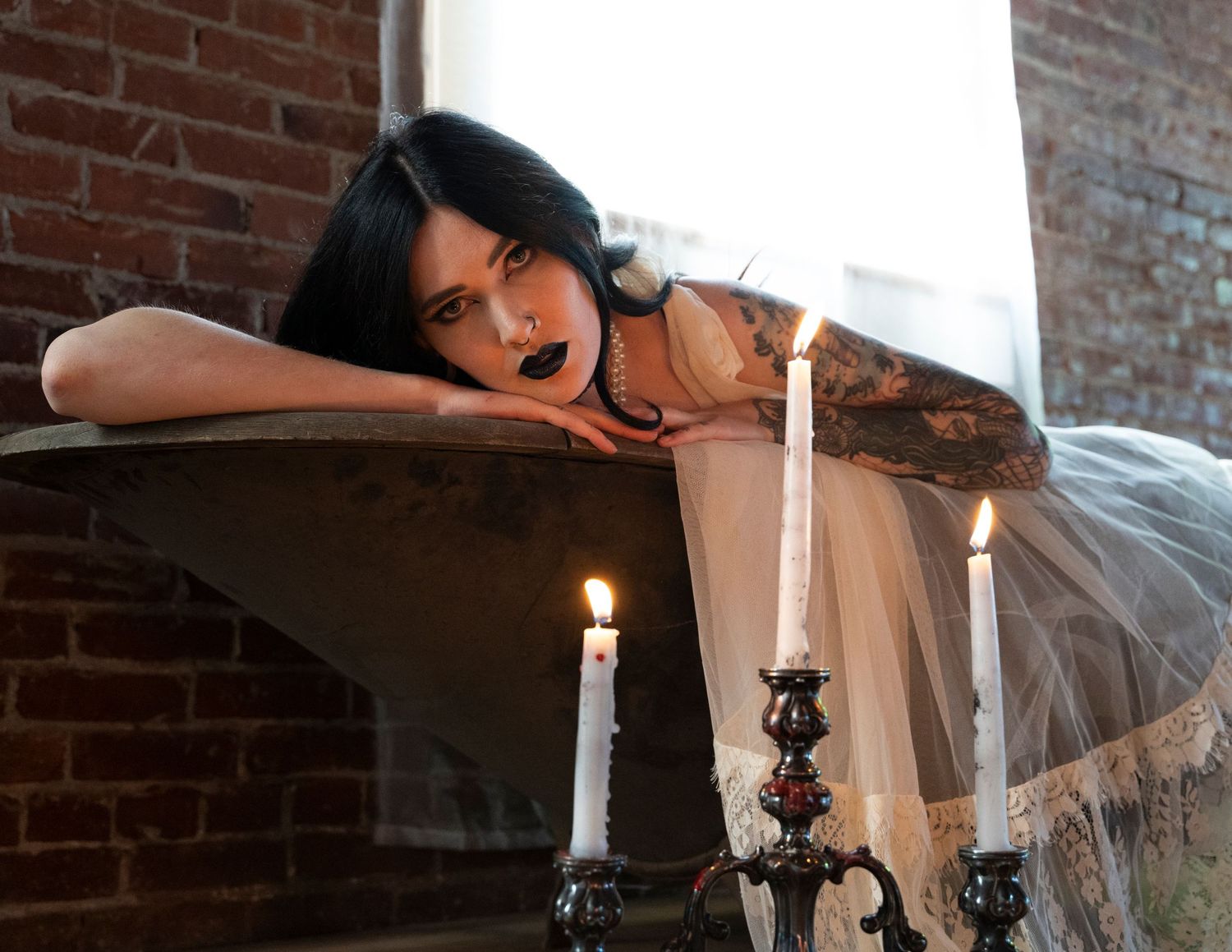 Gothic-inspired scene with candles and vintage bathtub in brick interior.
