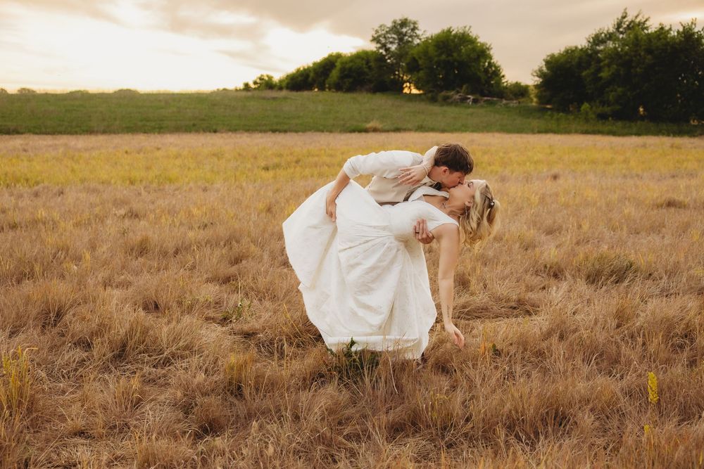 Groom dips bride for a romantic kiss in a golden field at sunset during outdoor wedding photography.