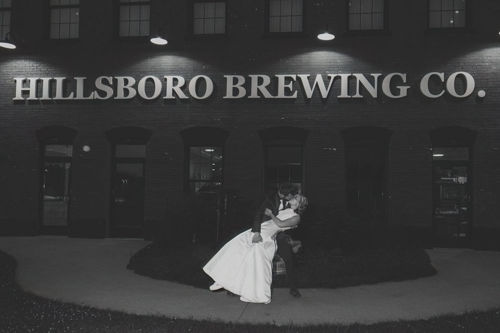 Black and white photo of a couple sharing a kiss outside Hillsboro Brewing Co. at night in wedding attire.