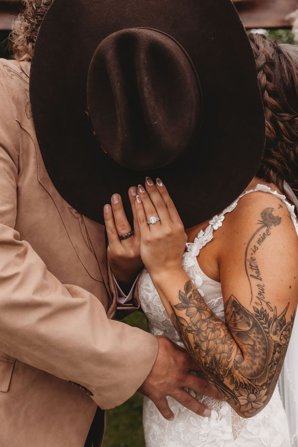 A romantic close-up shot of a couple embracing, with visible tattoos and a brown hat creating an intimate moment.