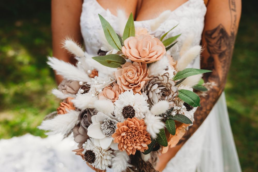 Elegant bridal bouquet featuring peach dahlias, white feathers, and eucalyptus leaves against a wedding dress.