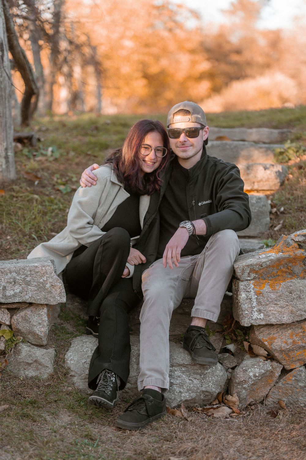 Couple sitting together on stone wall during autumn sunset.